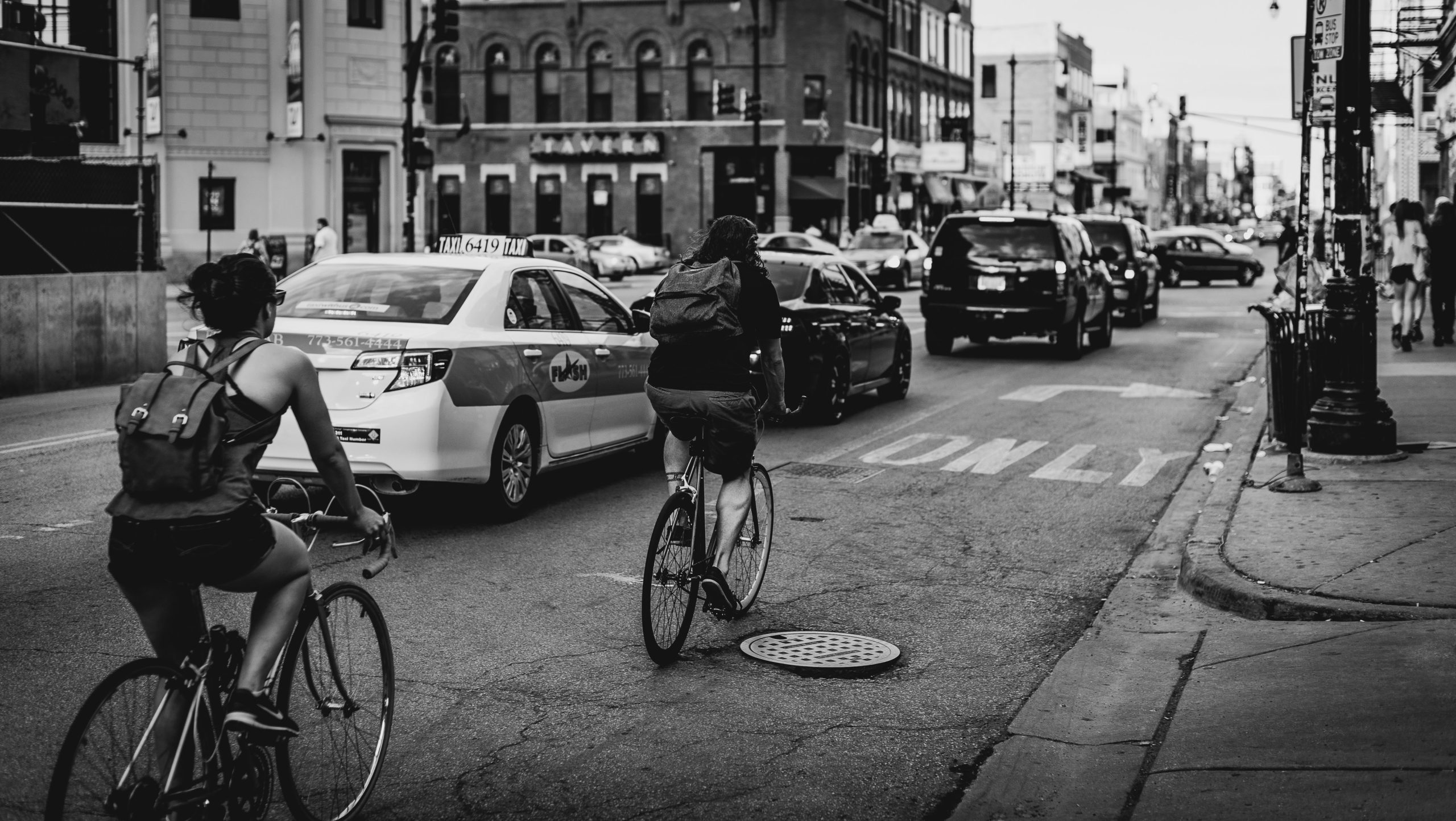 Black and white photo of a street in Chicago with cars and people on bicycles