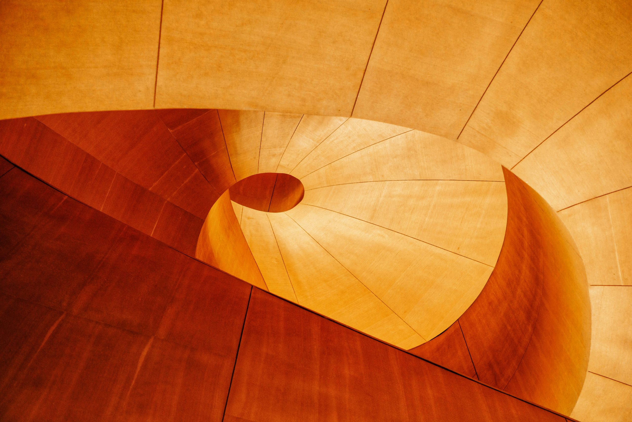 Photograph of a spiraling wooden staircase taken from underneath in natural light