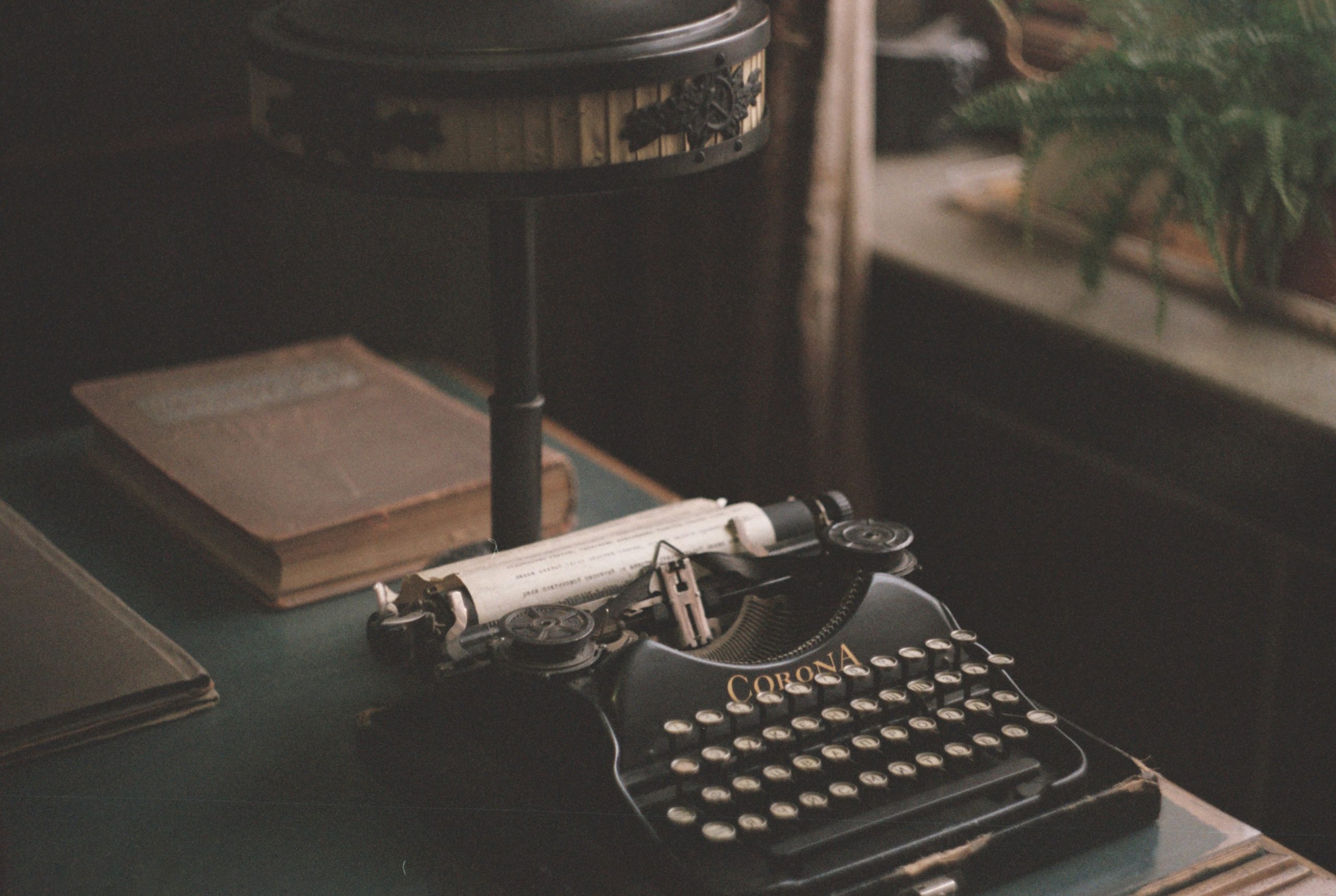 Photograph of an old typewriter on a desk with an old book behind it and sheet of paper inside