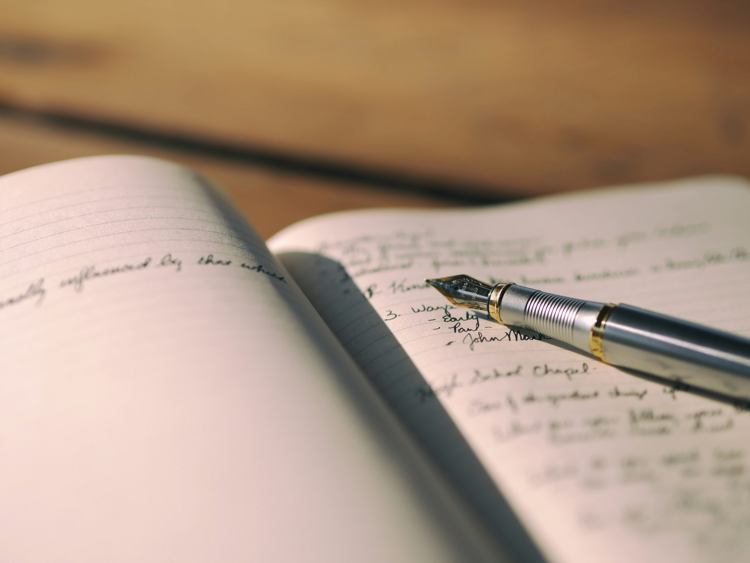 Photograph of a fountain pen laying on the page of a notebook with handwritten notes on it