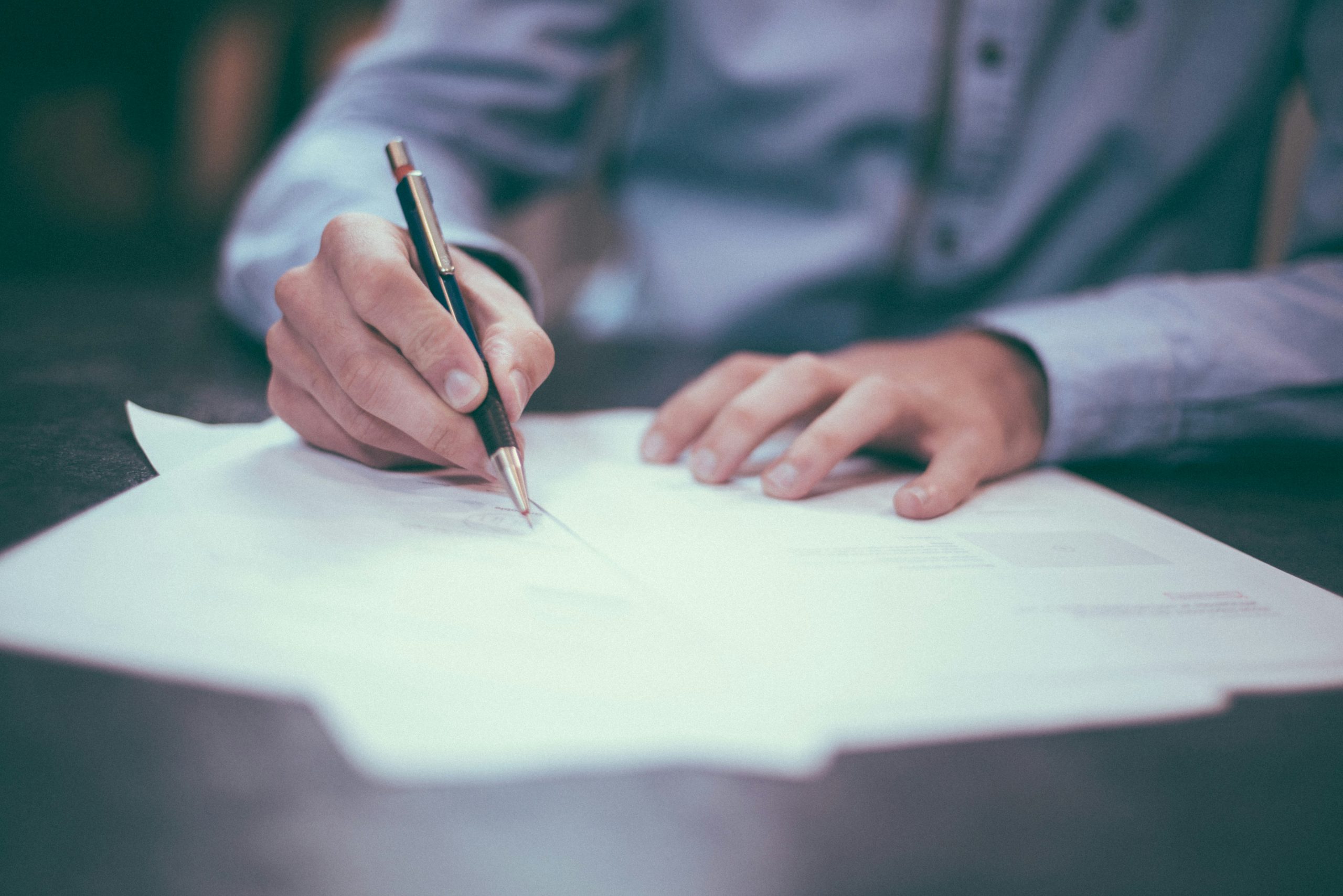 Photograph of a man holding a pen to sign a paper contract